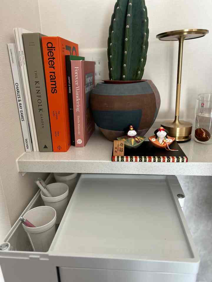 白と茶色のトーンの机の上の棚に観葉植物、ゴールドのテーブルランプ、日本の伝統的なオブジェが配置された落ち着いた雰囲気のインテリア