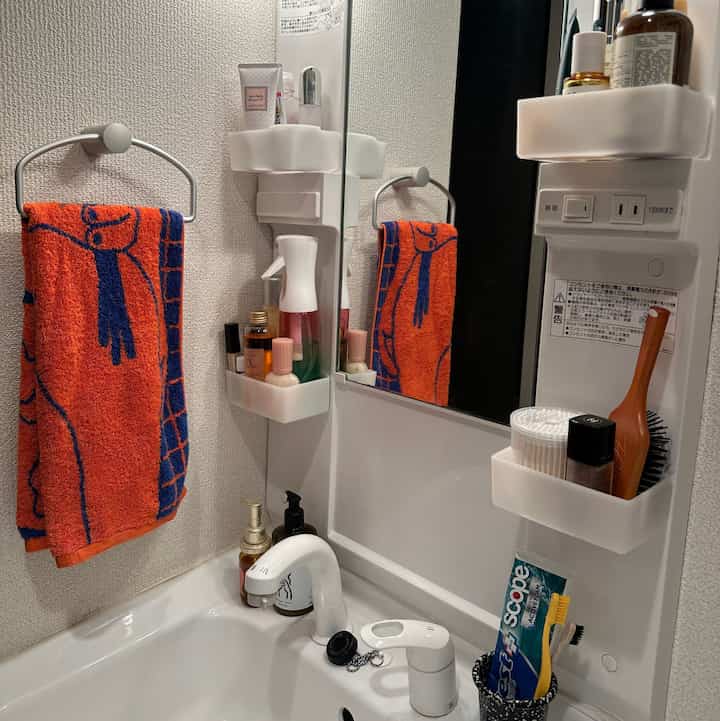 白い設備とオレンジのタオルが配置されたモダンな洗面台と整理された収納がある清潔感のあるバスルーム