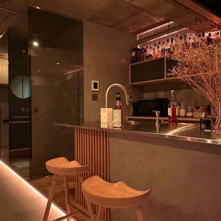 グレーのトーンでまとめられたモダンなキッチンダイニング、木目調のバースツールとドライフラワーが配置された雰囲気のある空間