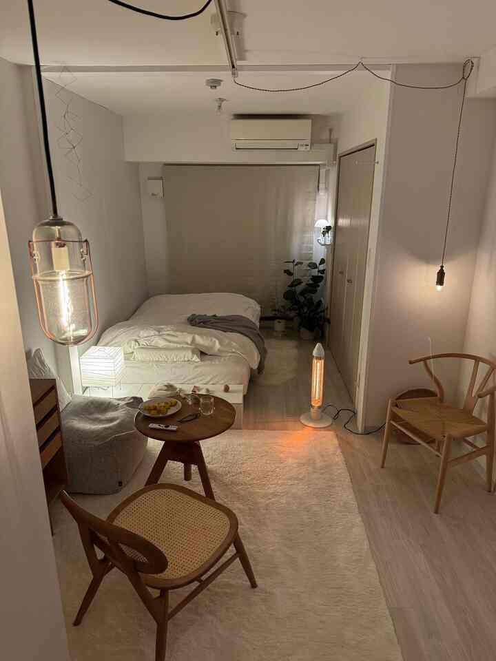 A cozy studio bedroom in white and natural brown tones, featuring natural material furniture and a large rug