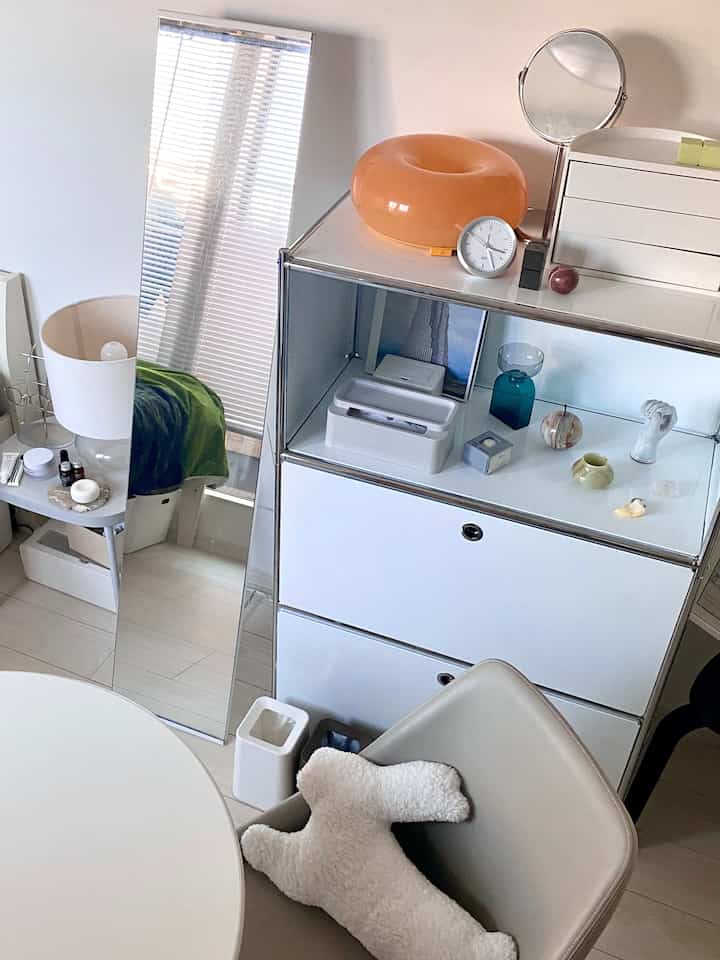 白とベージュのトーンが特徴的なモダンな韓国インテリア、収納キャビネットと丸テーブル、鏡が配置された雰囲気のある空間