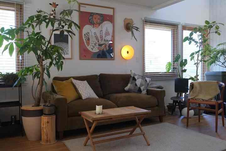 ナチュラルな色調のリビングルーム、茶色のソファと木製のコーヒーテーブル、壁にポスターと丸い壁付け照明が配置された落ち着いた空間