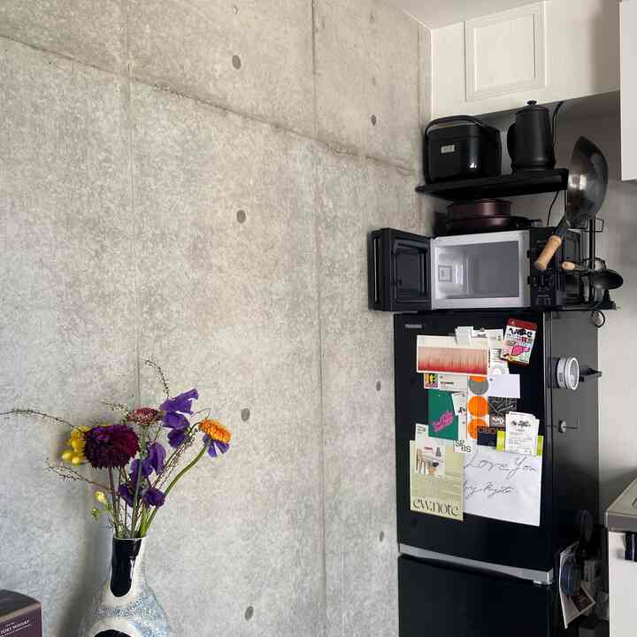 白と黒の家電があるキッチン、コンクリート壁と花瓶が配置されたモダンなインテリア