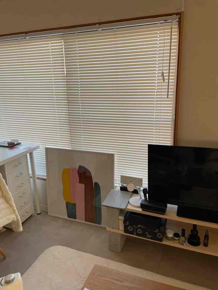 Compact living room with white blinds and wood tone furniture, featuring a colorful poster leaning against the wall, creating a cozy atmosphere