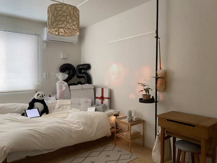 White and natural tone bedroom featuring a bed with a panda doll, small nightstand, and wooden furniture creating a cozy atmosphere