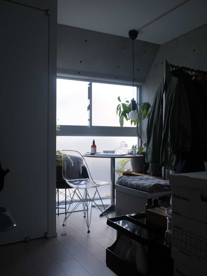 White-toned small studio home office with transparent chair, indoor plants, and organized storage creating a focused atmosphere