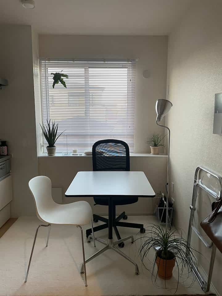 A compact home office space in white and black tones featuring a clean desk, office chair, and multiple plants with a modern atmosphere
