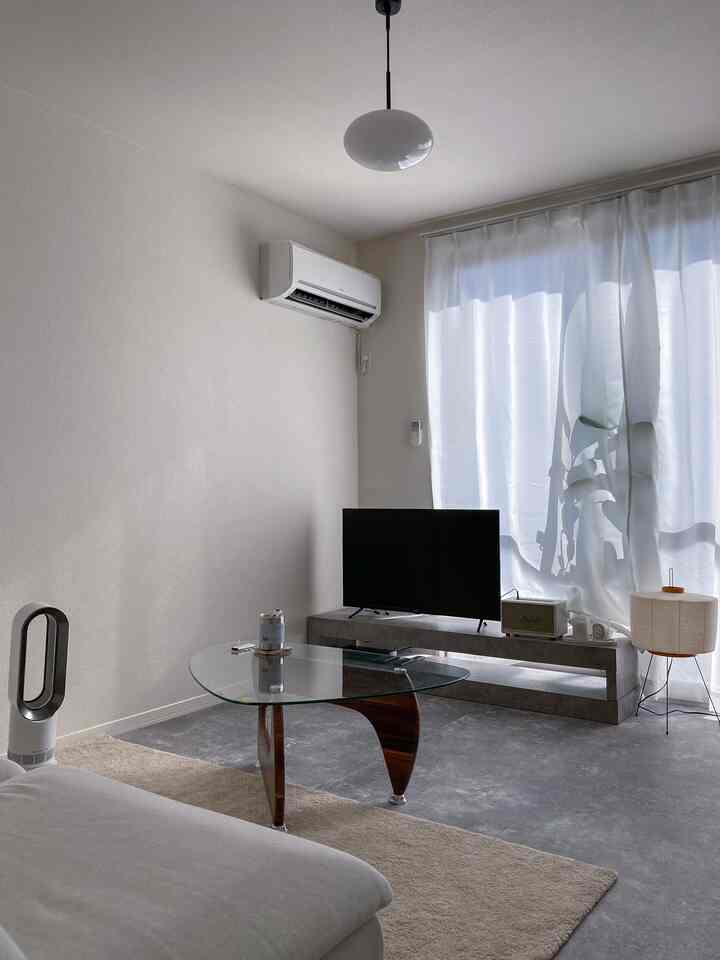 白とライトグレーのトーンの一人暮らしリビング、シンプルモダンスタイルでガラスのコーヒーテーブルとフロアランプが配置された清潔感ある空間