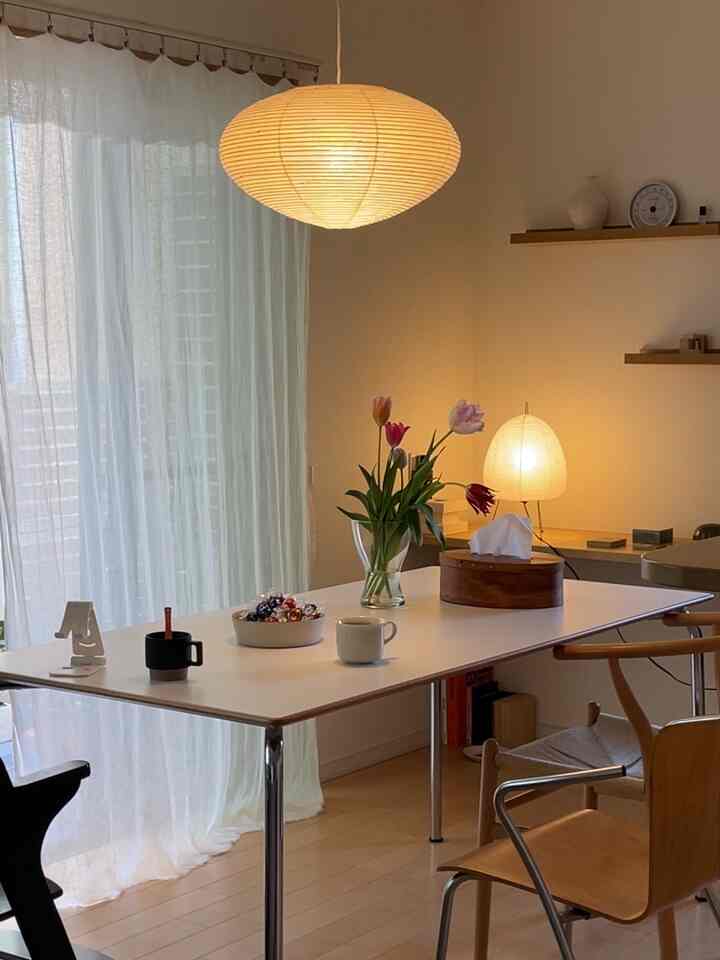 ナチュラルな木目調と白を基調としたダイニングルーム、テーブル上の花瓶と照明が配置された雰囲気のあるインテリア