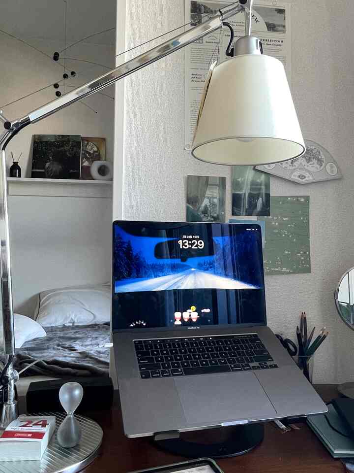 白とグレー調のワンルームホームオフィス、テーブルランプとノートパソコンが置かれたシンプルなデスク空間