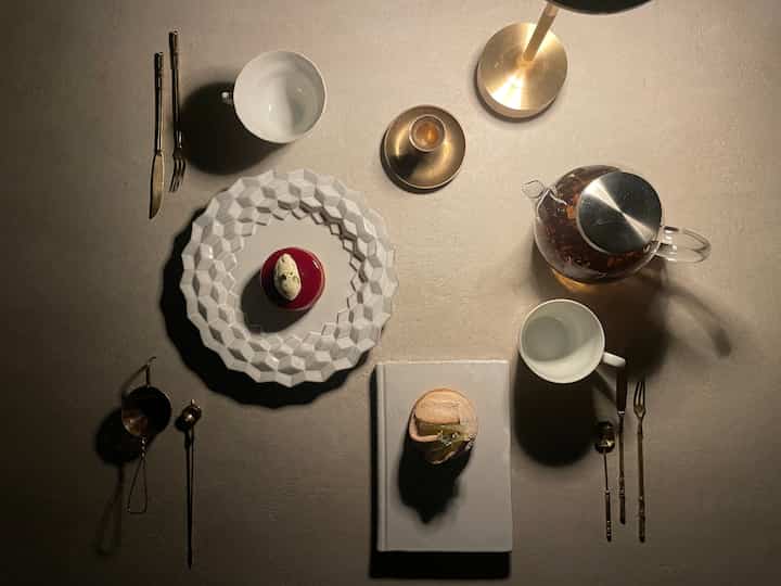 Beige-toned table with Astier de Villatte plate and cakes, brass table lamp and tea accessories in a minimalist home cafe setting