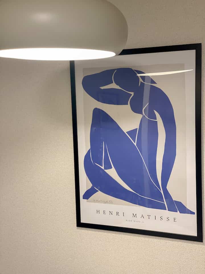 明るいベージュの壁と白い照明があるダイニングの壁に、青いヌードの絵が額縁に入って飾られている雰囲気のあるインテリア