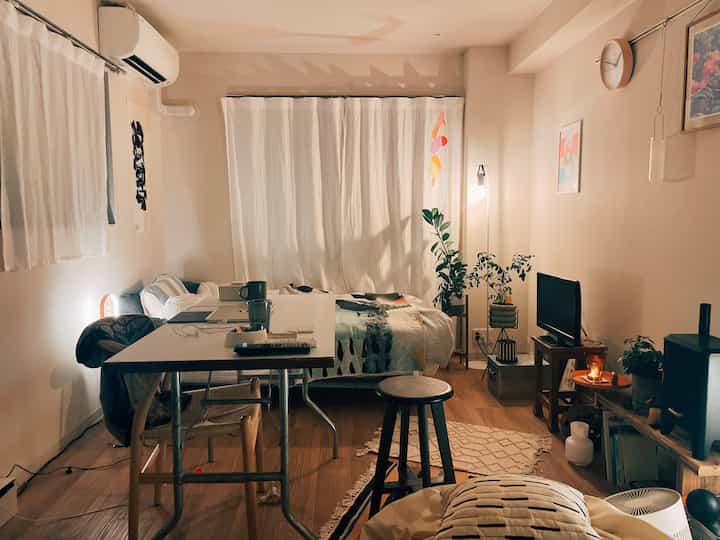 Warm beige bedroom and home office space with bed, desk, and plants arranged for a cozy atmosphere