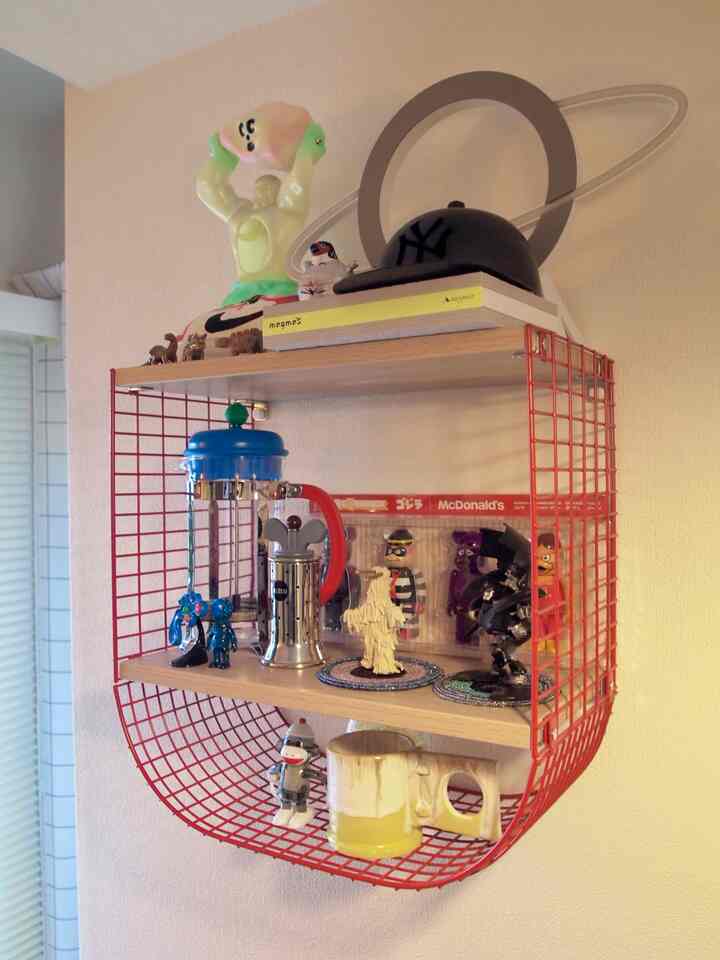 赤い金属フレームとナチュラルな木製の棚が壁に設置され、さまざまな装飾品やコーヒー用具が並ぶ印象的なインテリア