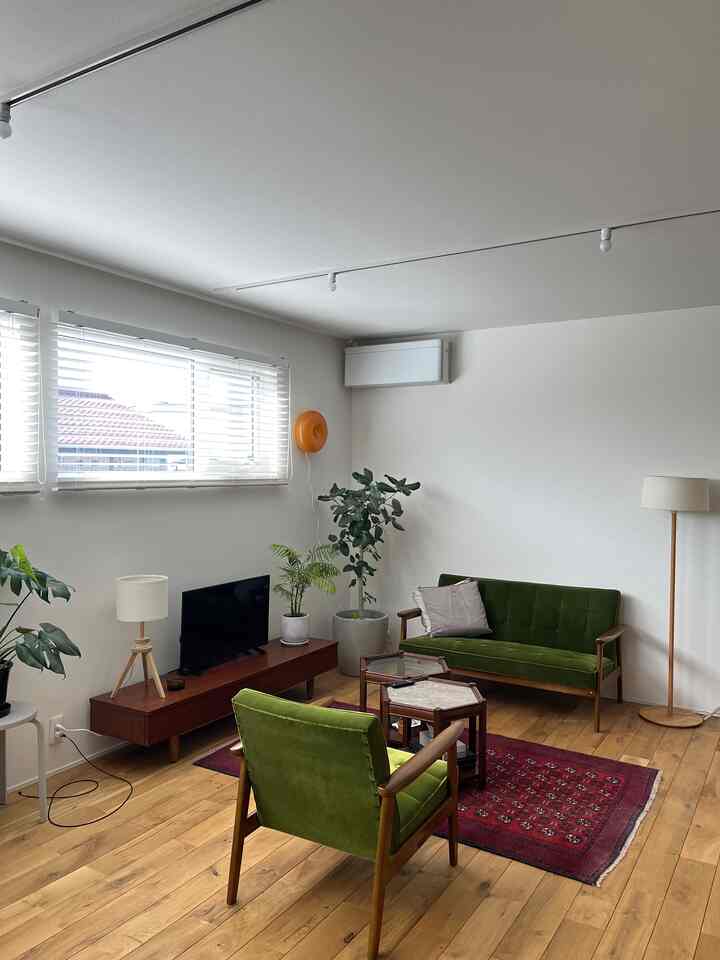 ナチュラルな色調のリビングルーム、緑のヴィンテージソファと赤いヴィンテージラグが配された雰囲気のある空間