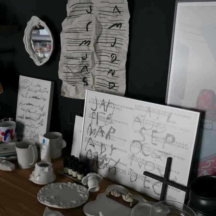 黒い背景の壁と白い額縁のアートポスターが木製のテーブルの上に並び、多様な陶器の小物が配置された雰囲気のあるホームギャラリー空間