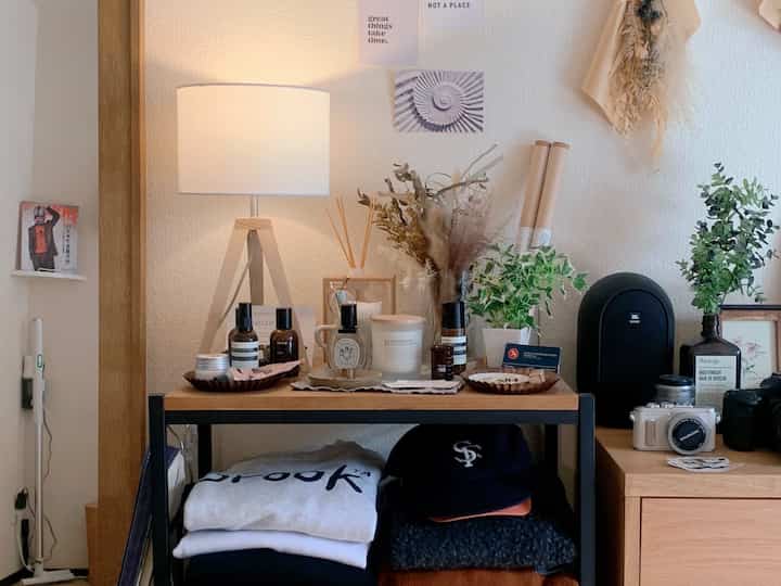 白い壁と木目調家具が調和する小さな玄関、テーブルランプと植物が温かい雰囲気を演出するインテリア