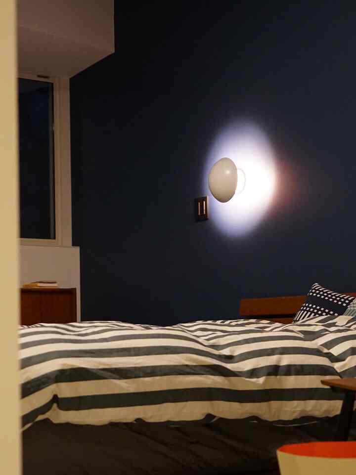 深いネイビーの壁紙、ストライプのベッドカバー、木製ベッドフレームが配置された落ち着いた寝室