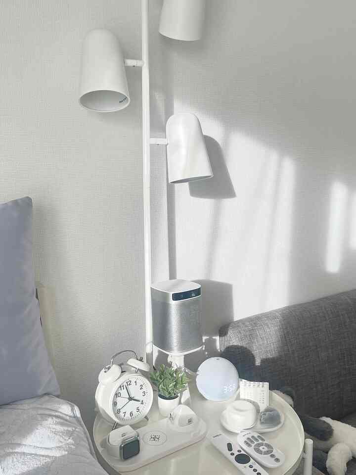 ホワイトとグレーのトーンでまとめられた1Kの一人暮らしの部屋、サイドテーブルに多様なデジタル機器とアナログ時計が配置されたホテルライクな空間
