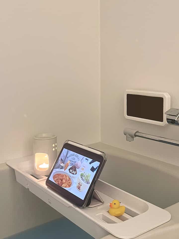 Bright white-toned bathroom bathtub featuring a white tray with aroma candle and tablet setup, creating a minimal single household vibe