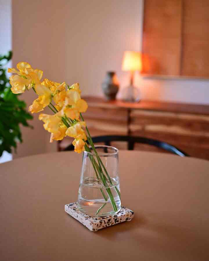 ベージュのダイニングルーム、クリアな花瓶とテラゾーのコースターが配置された自然で温かみのあるインテリア