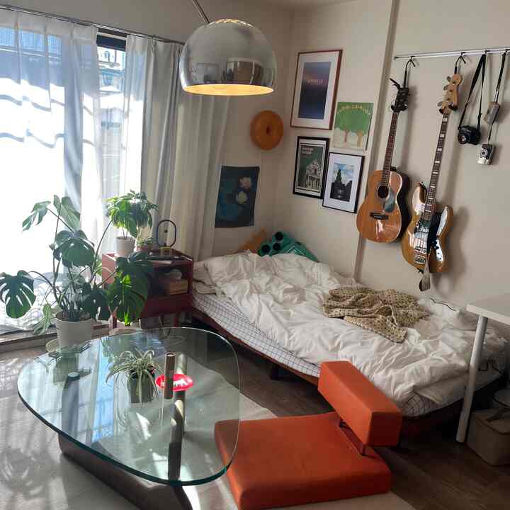 白と茶色のトーンの小さな寝室、ベッドとガラス製のコーヒーテーブル、多数の植物が配置されたナチュラルモダンなインテリア