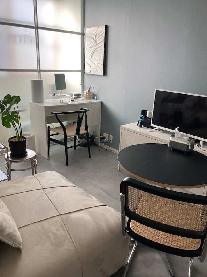 Modern living room in white and black tones featuring a computer desk with rattan chair and round table in a simple setting