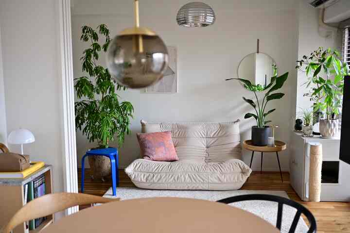 White-walled natural toned living and dining area featuring beige sofa and round dining table with greenery accents