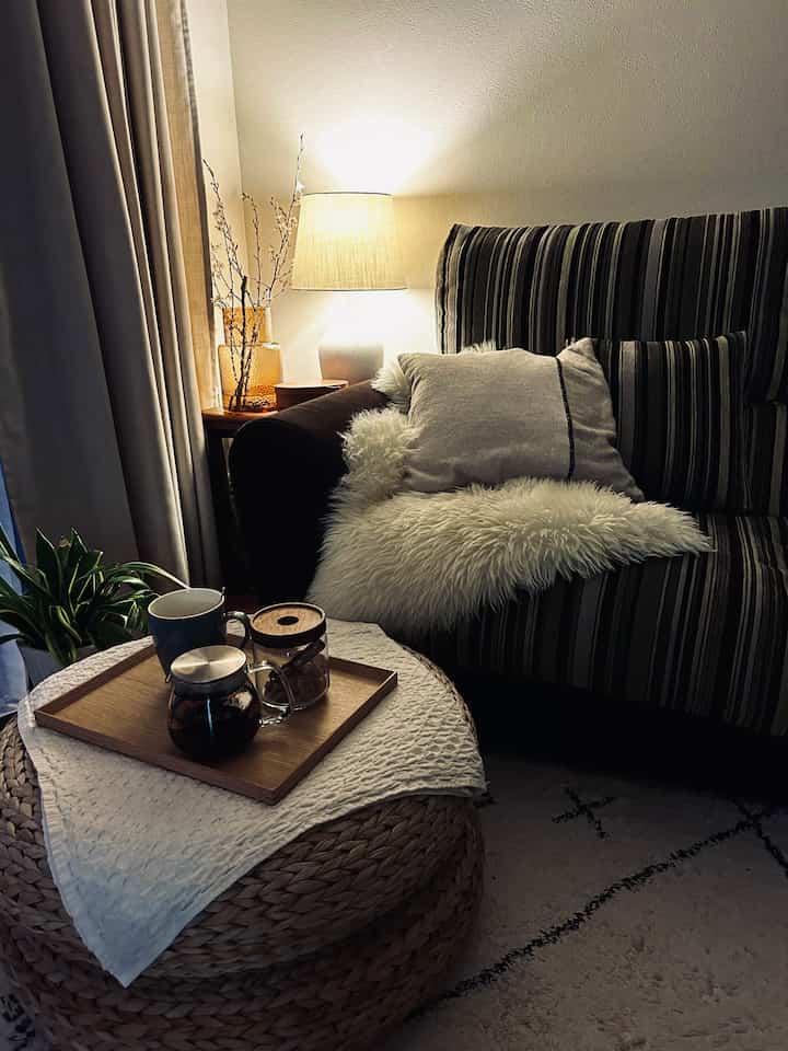 Beige and brown toned living room featuring striped sofa and rattan stool with wooden tray and tea set, creating a cozy atmosphere
