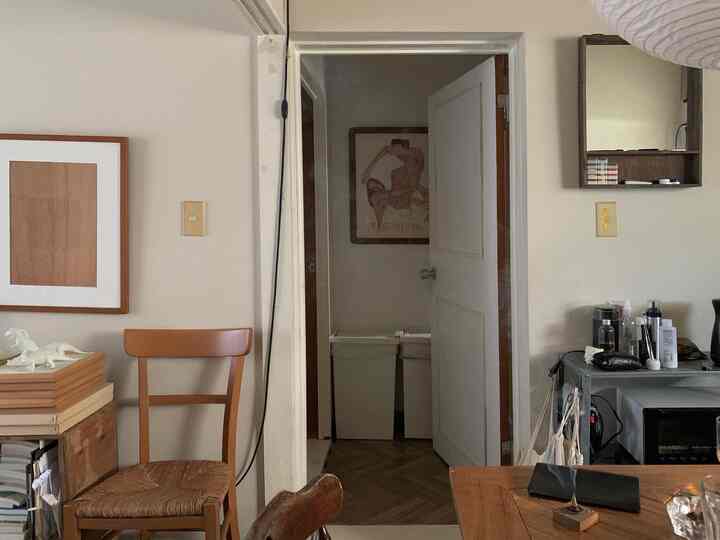 ナチュラルな色調のリビングと廊下、木製の椅子とテーブル、ポスターが配置された雰囲気のあるインテリア