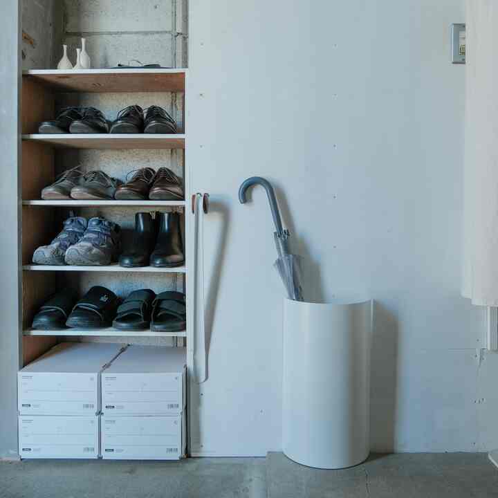 白を基調としたすっきりとした玄関、シューズラックと傘立てが配置されたミニマルでモダンな空間