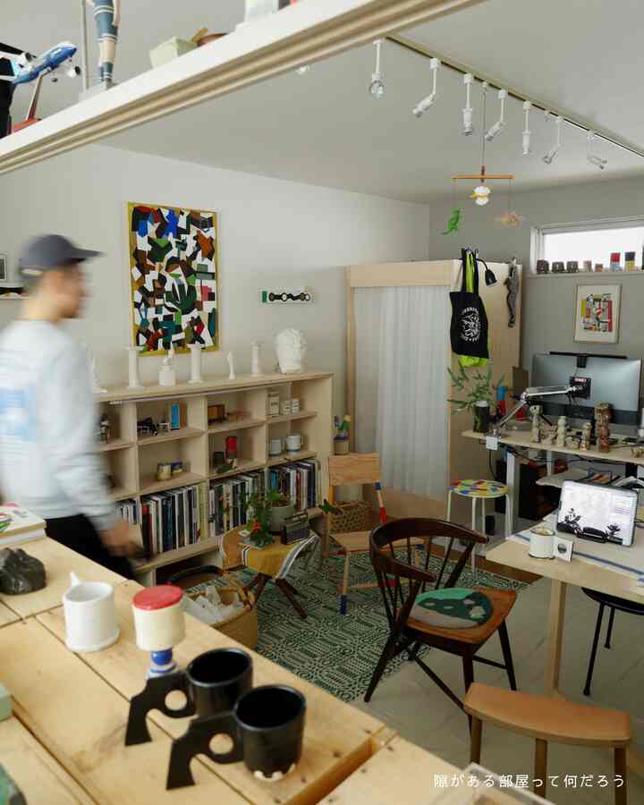A cozy single household workspace with white walls, wood-toned furniture, bookshelves, and a green rug