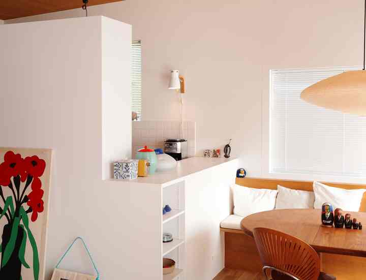 A white and wood tone Nordic style dining room and kitchen space featuring a pendant light and bench seating with a cozy atmosphere