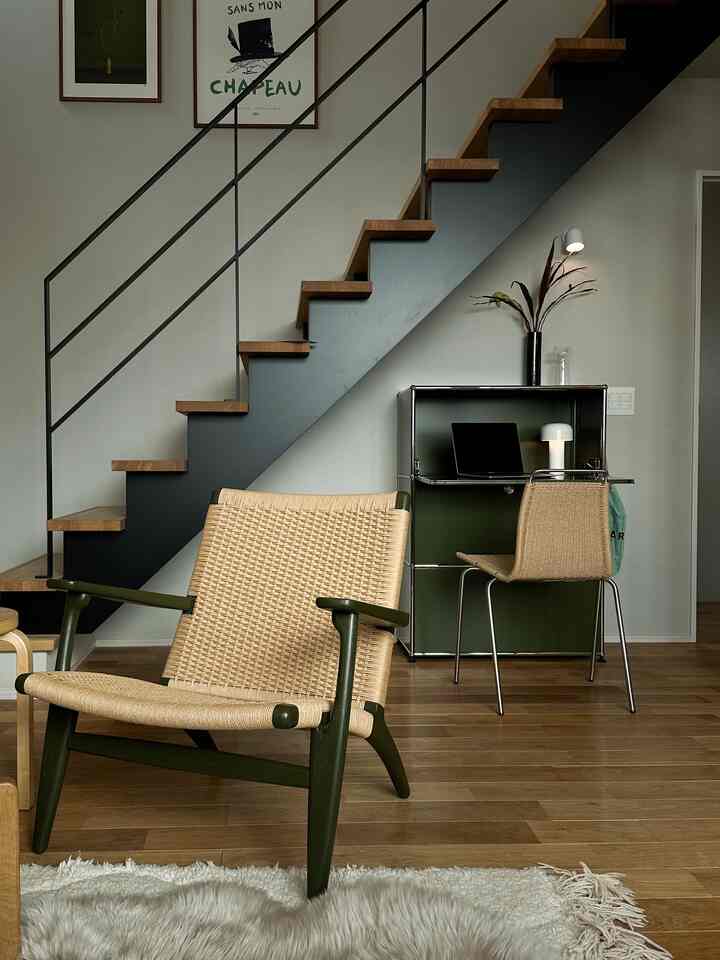 Modern home office space with natural colors and wood tones, featuring an armchair and desk placed under the staircase.