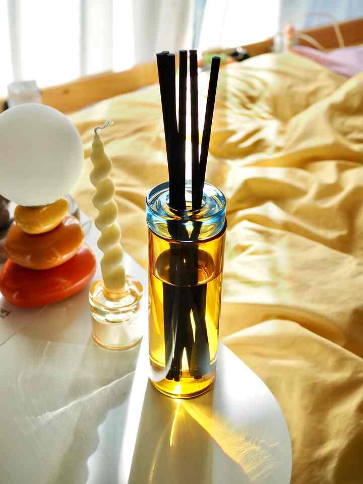 黄色い掛け布団カバーの寝室、テーブル上にキャンドルとディフューザーが置かれた温かく落ち着いた雰囲気のあるインテリア