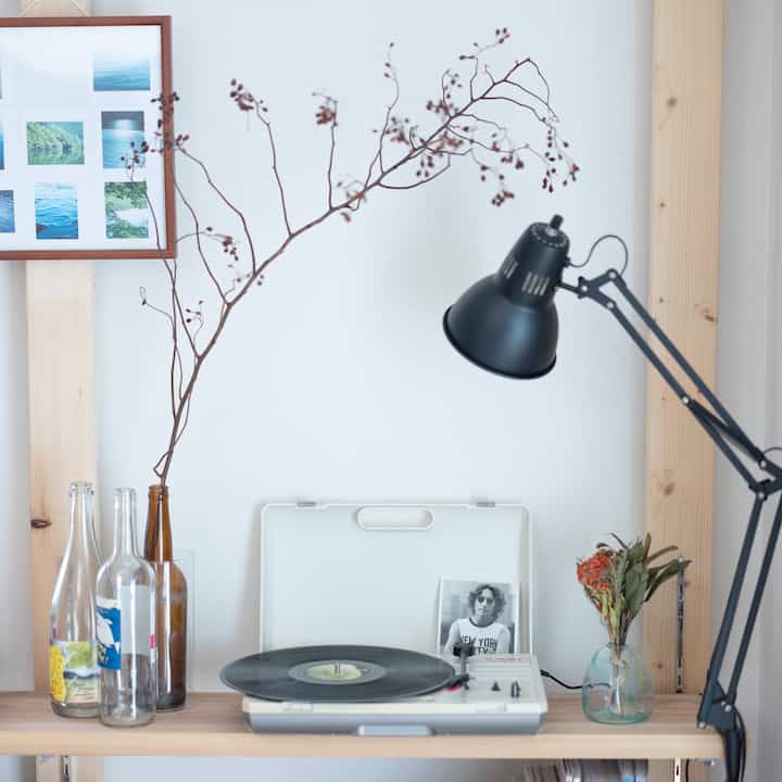 白い壁とナチュラルな木目調のデスクにテーブルランプや空の瓶、レコードプレーヤーが置かれたシンプルなインテリア