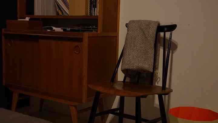 暖かみのある木目調と黒を基調とした北欧スタイル寝室、折りたたまれたラプアンカンクリのブランケットとファネットチェアが配置された印象的な空間