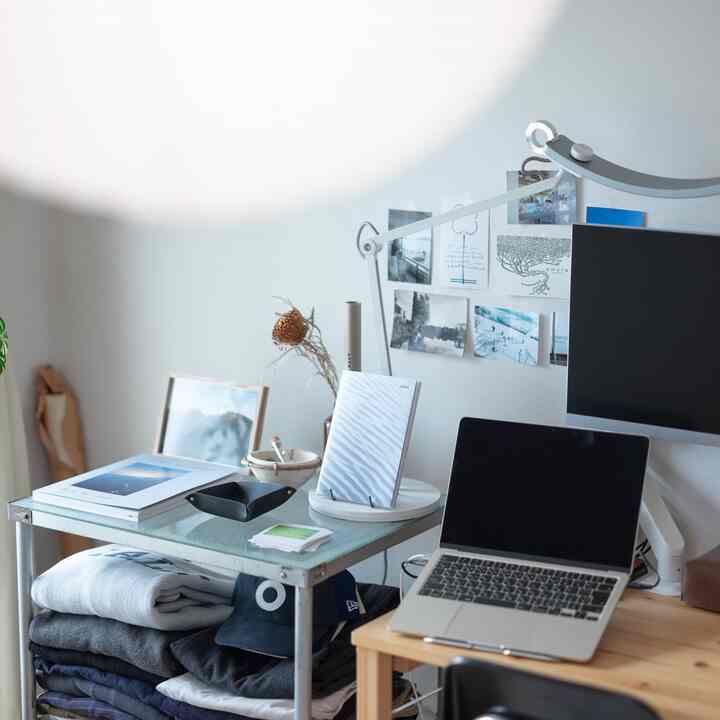 白い壁とナチュラルな木の机が配置されたコンパクトなホームオフィス、ノートパソコンとモニターが置かれた清潔感のある作業空間