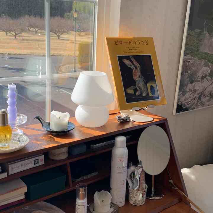 白と木目調が調和した寝室のナイトテーブルにテーブルランプとキャンドル、ポスターが配置された雰囲気のある空間