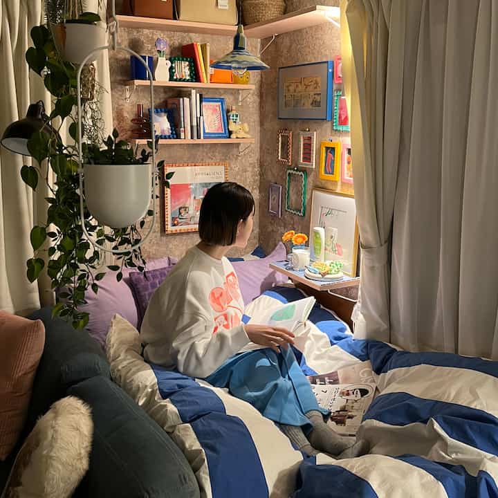 ブルーとホワイトのストライプ掛け布団カバーの寝室、書棚と額縁が配置された一人暮らしの読書空間