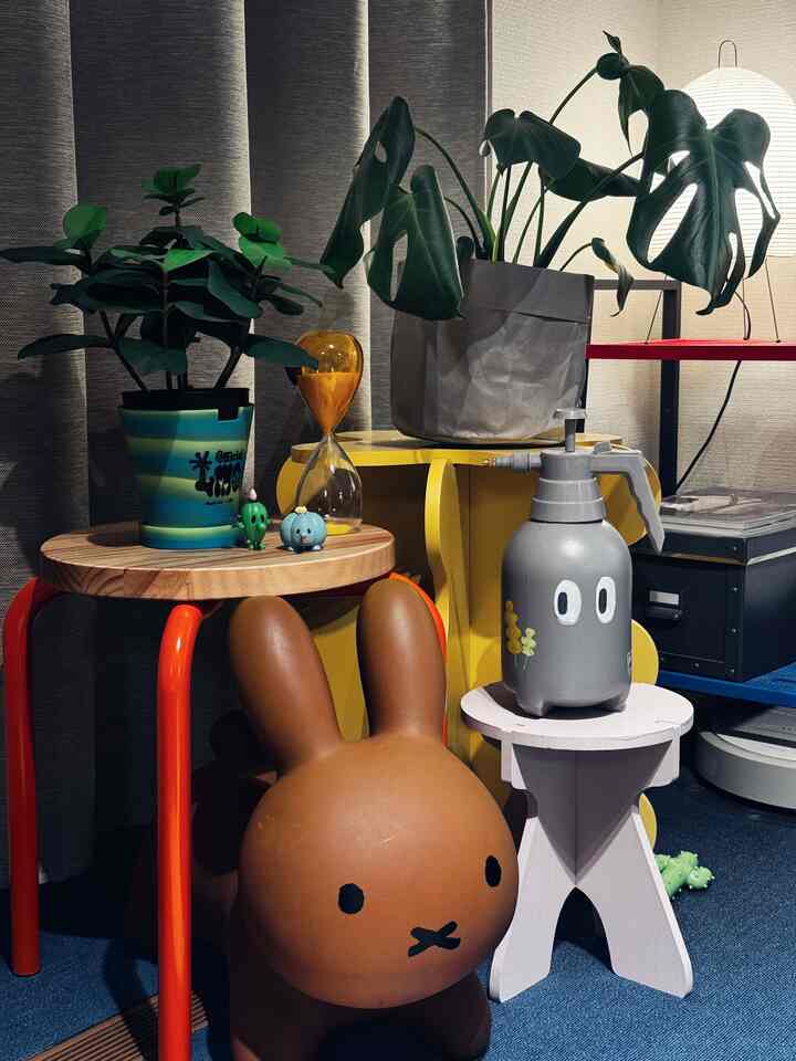 ナチュラルなブラウンとイエローの色調の室内コーナーで、植物とスツール、かわいいウサギ型の椅子が配置された印象的な空間