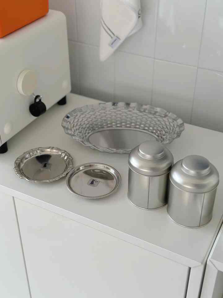 Silver-colored tableware and metal storage containers arranged neatly on a clean kitchen counter