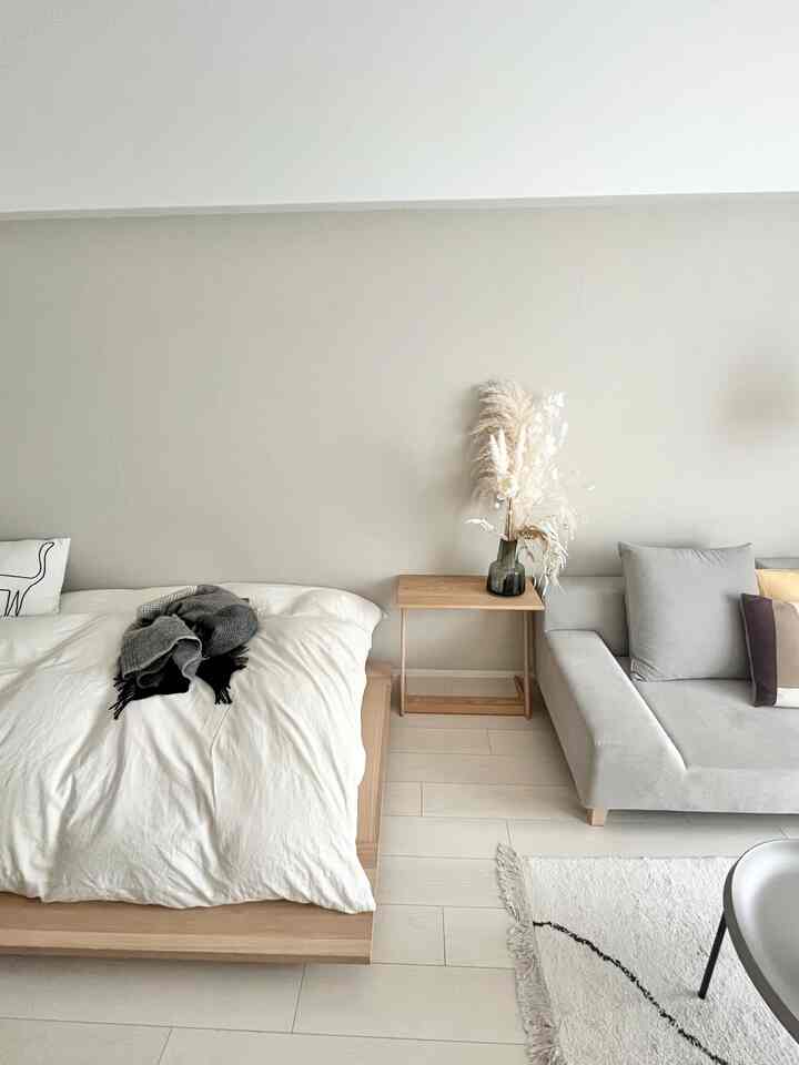 ナチュラルな色調の寝室とリビングが一体となった空間、ベージュの壁と明るい木製家具が落ち着いた雰囲気を醸し出すインテリア