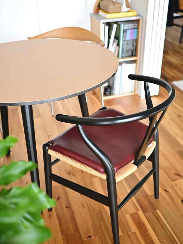 バーガンディのクッションが置かれたブラックフレームのカールハンセンのダイニングチェアと円形のダイニングテーブルが配置されたナチュラルな印象のキッチンスペース