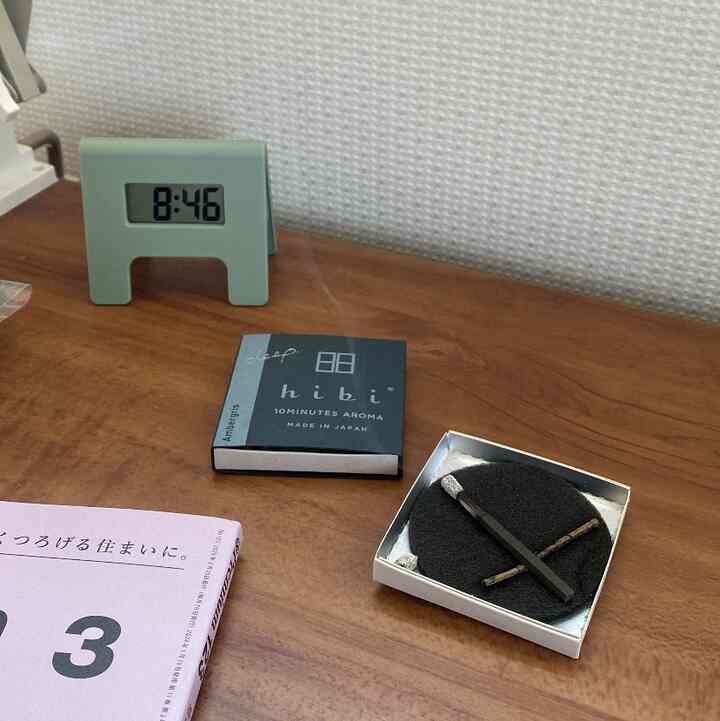 白い壁と茶色の机にデジタル時計とアロマ小物が配置されたシンプルで落ち着いたインテリア