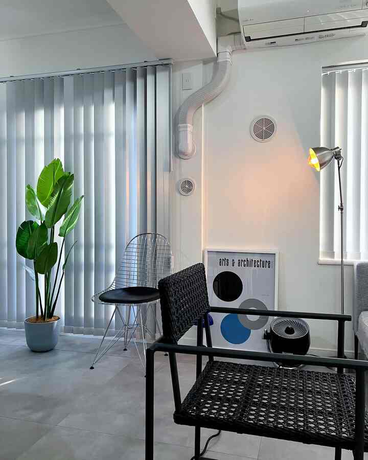 モノトーンのリビングスペース、シンプルな椅子とフロアランプ、大きなフェイクグリーンが配置された清潔感のあるインテリア