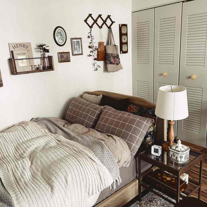 ナチュラルなブラウンとホワイトの色調の寝室、ブラウンのベッドとナイトテーブル、テーブルランプ、壁デコが配置された雰囲気のあるヴィンテージ空間