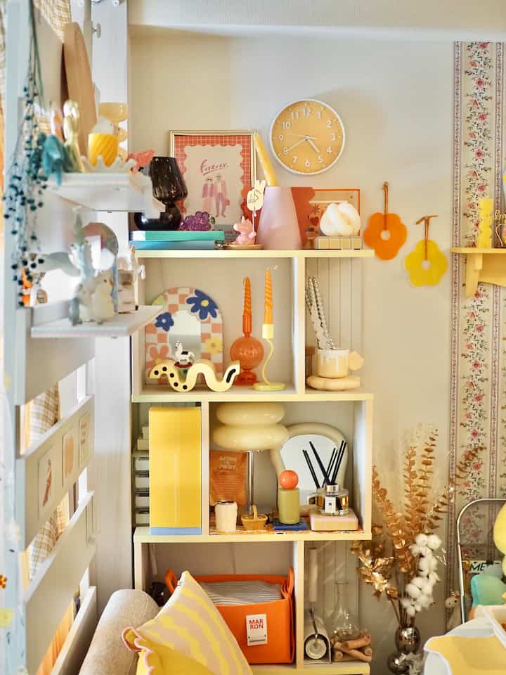 明るい黄色の色調のリビング、白い棚にカラフルな装飾品とキャンドルが配置された雰囲気のある空間
