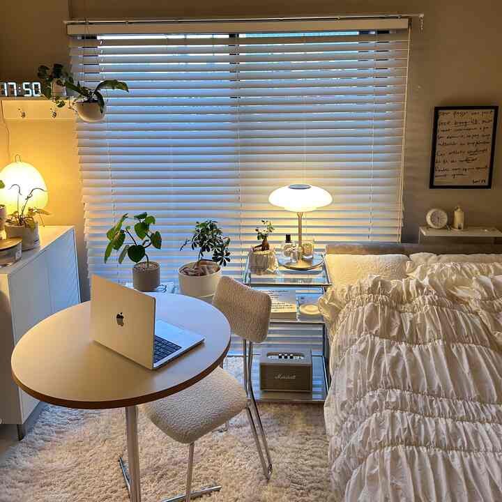 White and beige toned studio bedroom featuring round dining table and side table with a cozy and calm atmosphere