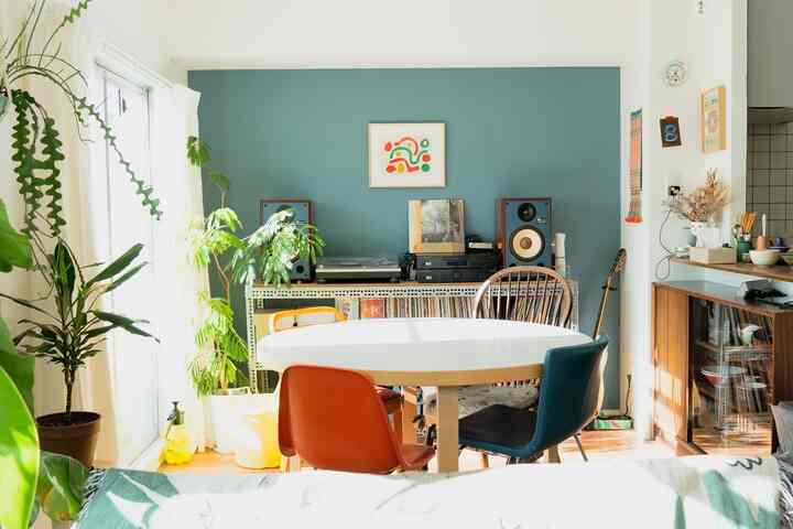 青いアクセントウォールが特徴的なリビング、中央に白い楕円形のダイニングテーブルと多様な色の椅子が配置された雰囲気のあるインテリア。